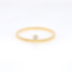 Minimalist diamond ring with a single off-center round diamond on a thin fine gold band.