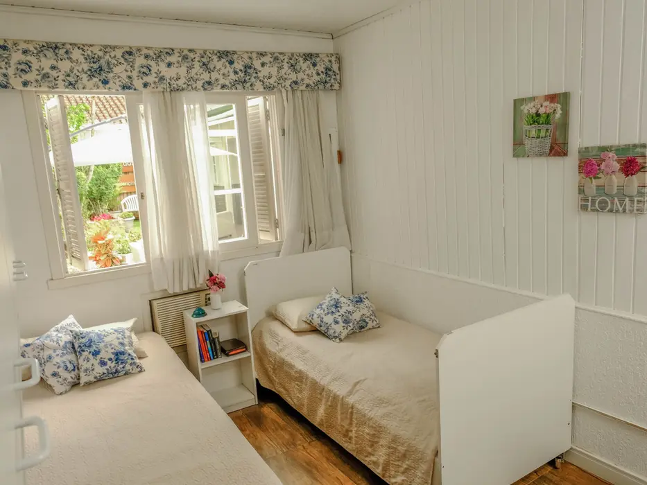 Quarto com duas camas em brancos com camas de solteiro, janelas com cortinas e um quadro com a palavra 'home'