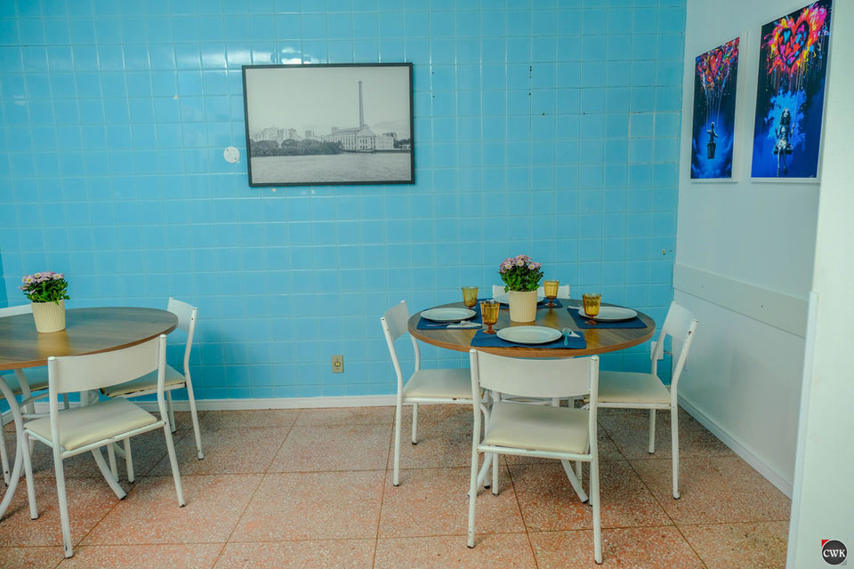 Mesa de jantar com quatro cadeiras, pronta para uma refeição, em uma sala com paredes azuis e duas fotos na parede.