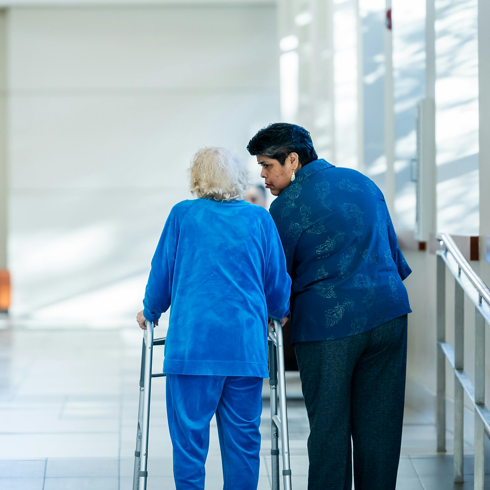 Caregiver assisting elderly woman with a walker in a hallway