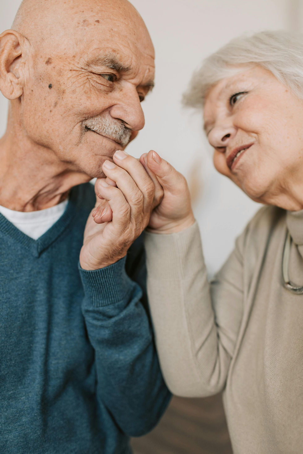 Elderly couple holding hands and smiling at each other.