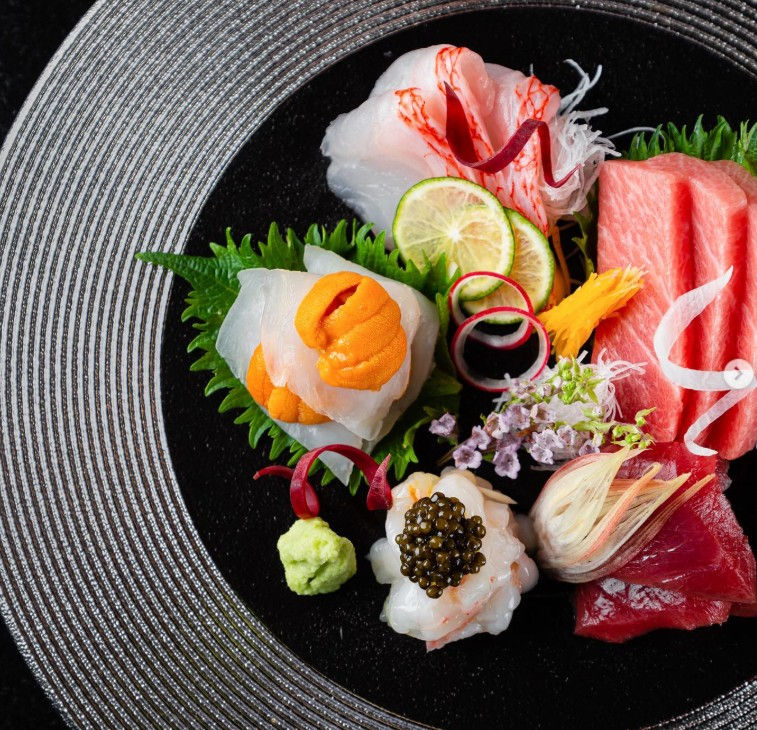 The food at TakaHisa is structured around a progression of seafood-focused dishes, supported by carefully selected warm preparations. The menu images highlight a wide range of offerings that reflect both variety and consistency in quality. The experience often begins with lighter dishes such as Aj Sashimi Tataki Style, Mizu Tako Carpaccio, and Tuna Carpaccio with Truffle. Premium ingredients are introduced early, including Luxury Sea Urchin, Sea Urchin Box, and Caviar “Tradition”, reinforcing the restaurant’s emphasis on high-grade sourcing. Options such as Herbal Butter Grilled Scallop, Kinoko Shio Yaki, Unagi Tare Yaki, Saikyo Yaki, and Shin Shin Yaki introduce grilled textures and richer flavours. The use of truffle, uni, and caviar is consistent, but always controlled to support the main ingredient, making it one of the amazing restaurants in Banyan Tree Dubai. 