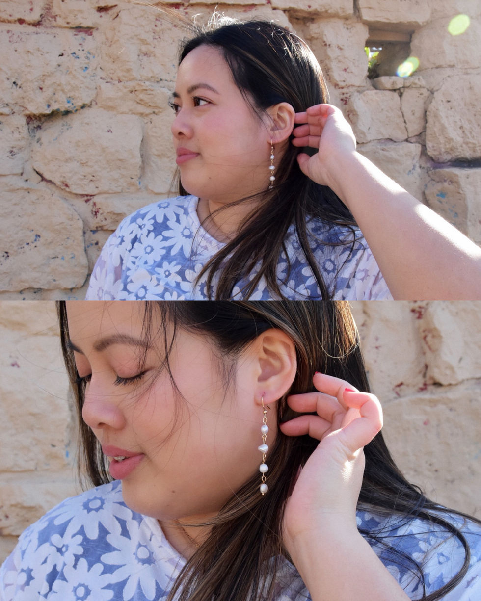 Eleanor is an Asian woman wearing a white daisy patterned top with short sleeves and her hair is blowing in the wind. She is wearing pearl drop earrings from kaolee shop.
