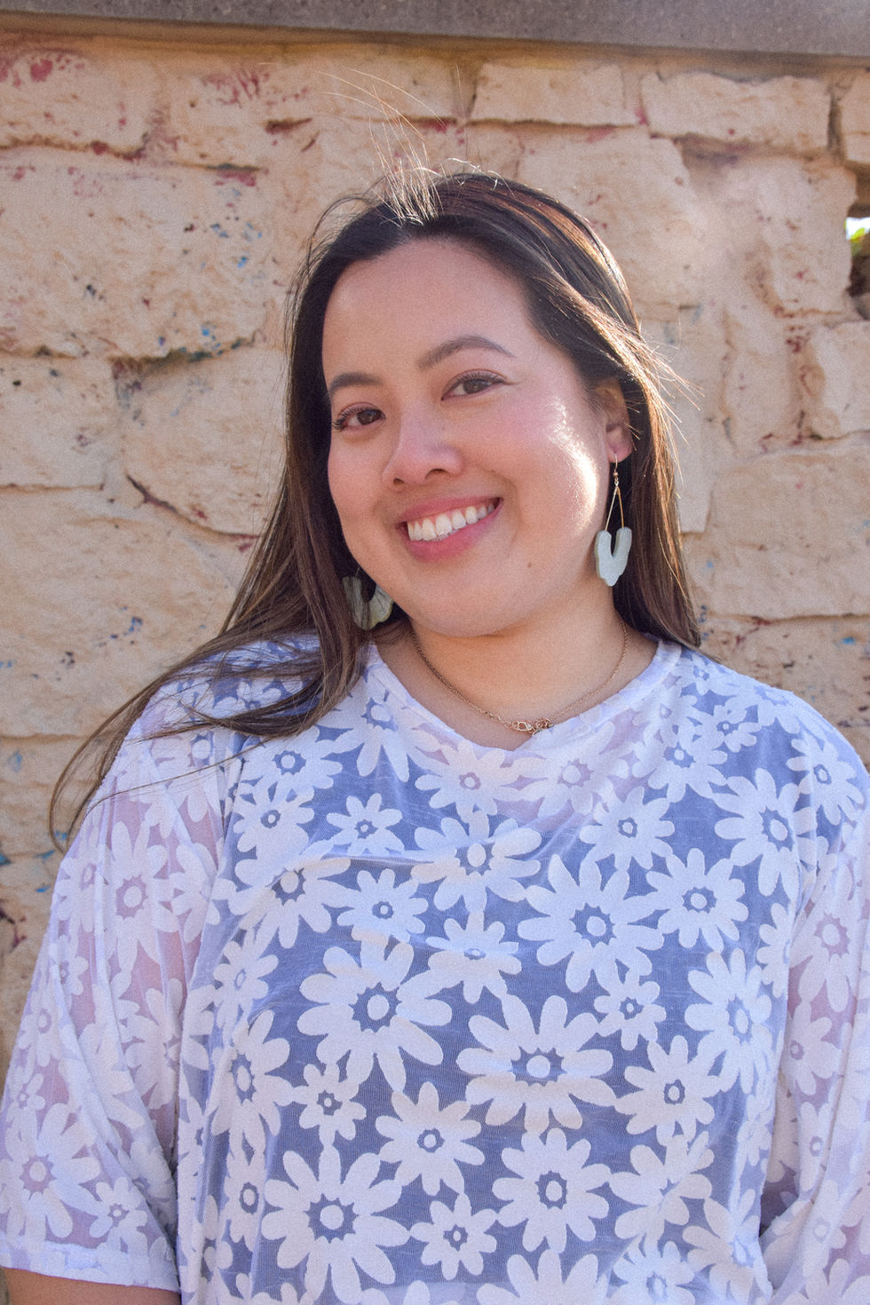 Eleanor is an Asian woman wearing a white daisy patterned top with short sleeves and her hair is blowing in the wind. She is wearing earrings from kaolee shop.