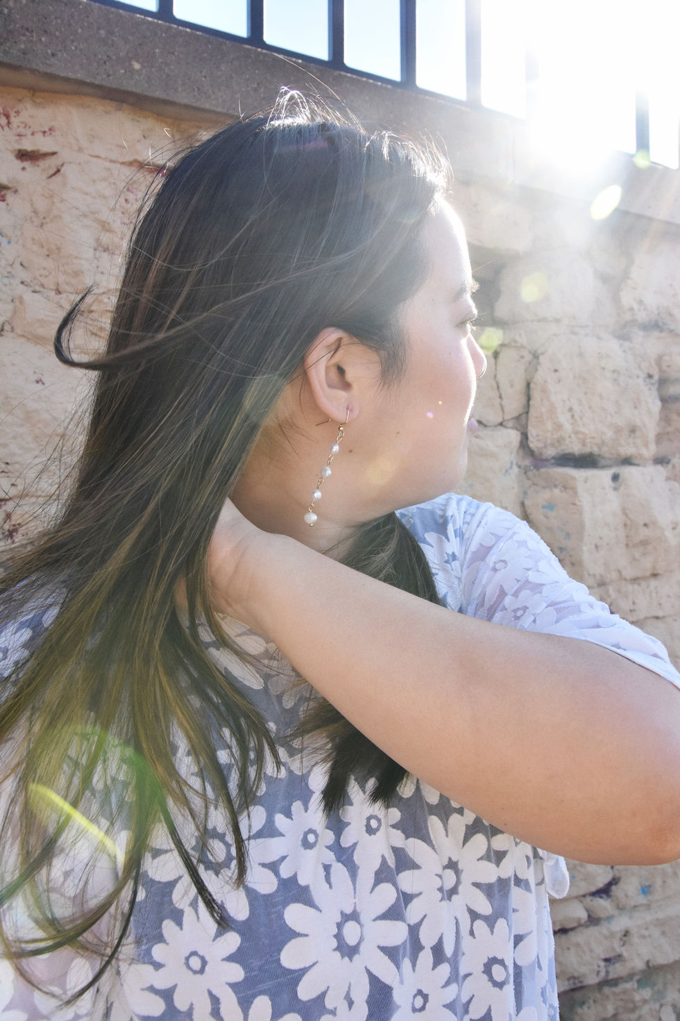 Eleanor is an Asian woman wearing a white daisy patterned top with short sleeves and her hair is blowing in the wind. She is wearing pearl drop earrings from kaolee shop.