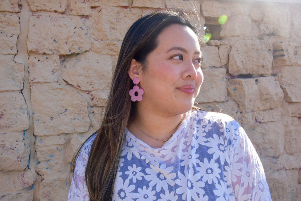 Eleanor is an Asian woman wearing a white daisy patterned top with short sleeves and her hair is blowing in the wind. She is wearing color changing daisy earrings from kaolee shop.