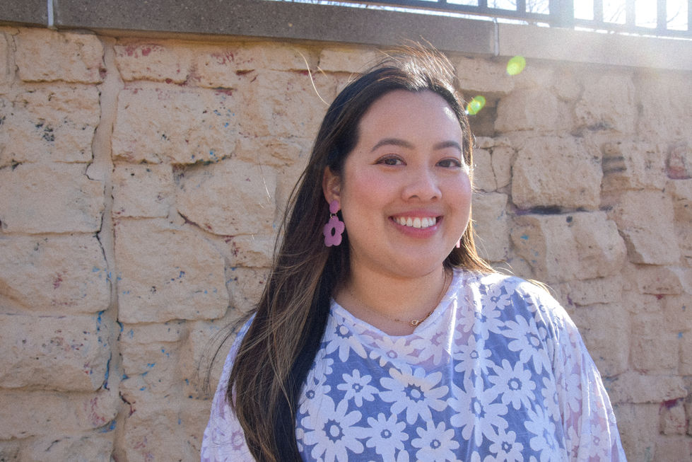 Eleanor is an Asian woman wearing a white daisy patterned top with short sleeves and her hair is blowing in the wind. She is wearing color changing daisy earrings from kaolee shop.