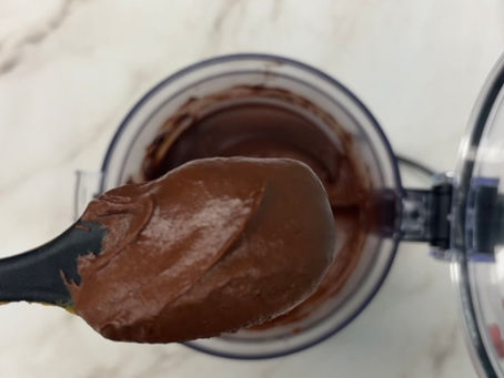 spatula with cream chocolate sweet potato frosting hovering over a food processor