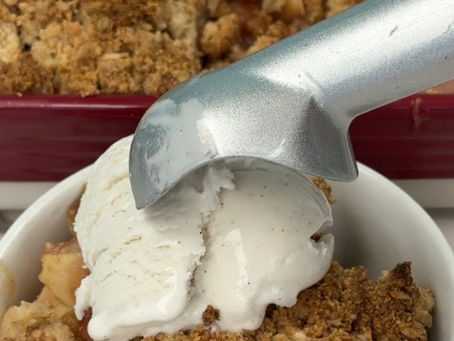 scooping vegan vanilla ice cream onto bowl of gluten free vegan apple berry rhubarb crumble