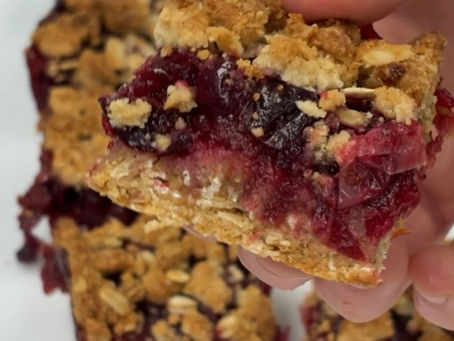 hand holding a cranberry filled crumble bar, with more pieces/squares in the background