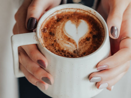 hands holding a warm cup of paleo hot cocao with a cute heart shape in the milk foam on top