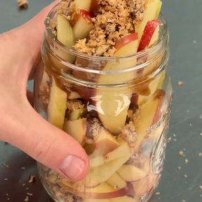 hand holding a jar filled with sliced apples, homemade coconut crunch topping, and date caramel sauce - a healthier viral caramel apple cup
