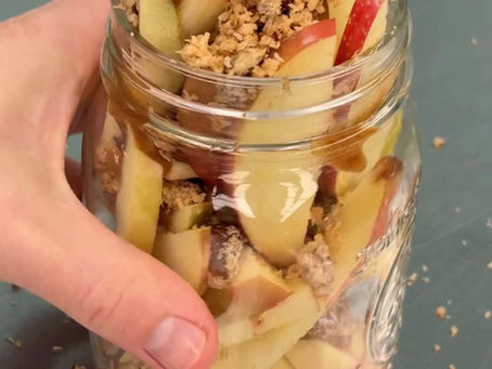 hand holding a jar filled with sliced apples, homemade coconut crunch topping, and date caramel sauce - a healthier viral caramel apple cup