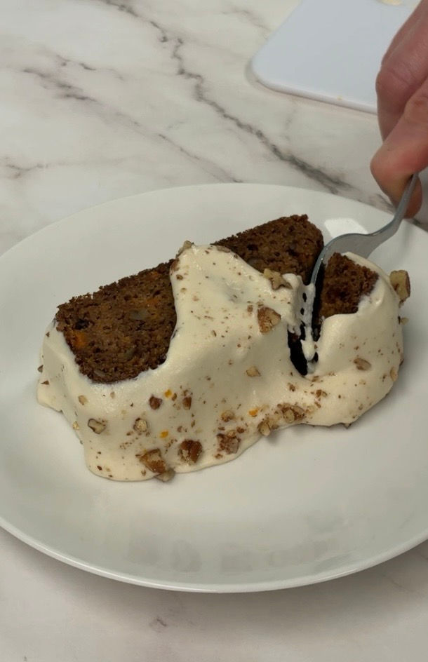 fork cutting into a slice of carrot cake loaf, topped with cashew cream cheese
