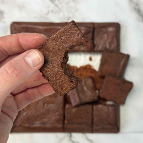hand holding a square piece of chocolate cake, above a square tray of gluten free chocolate snack cake