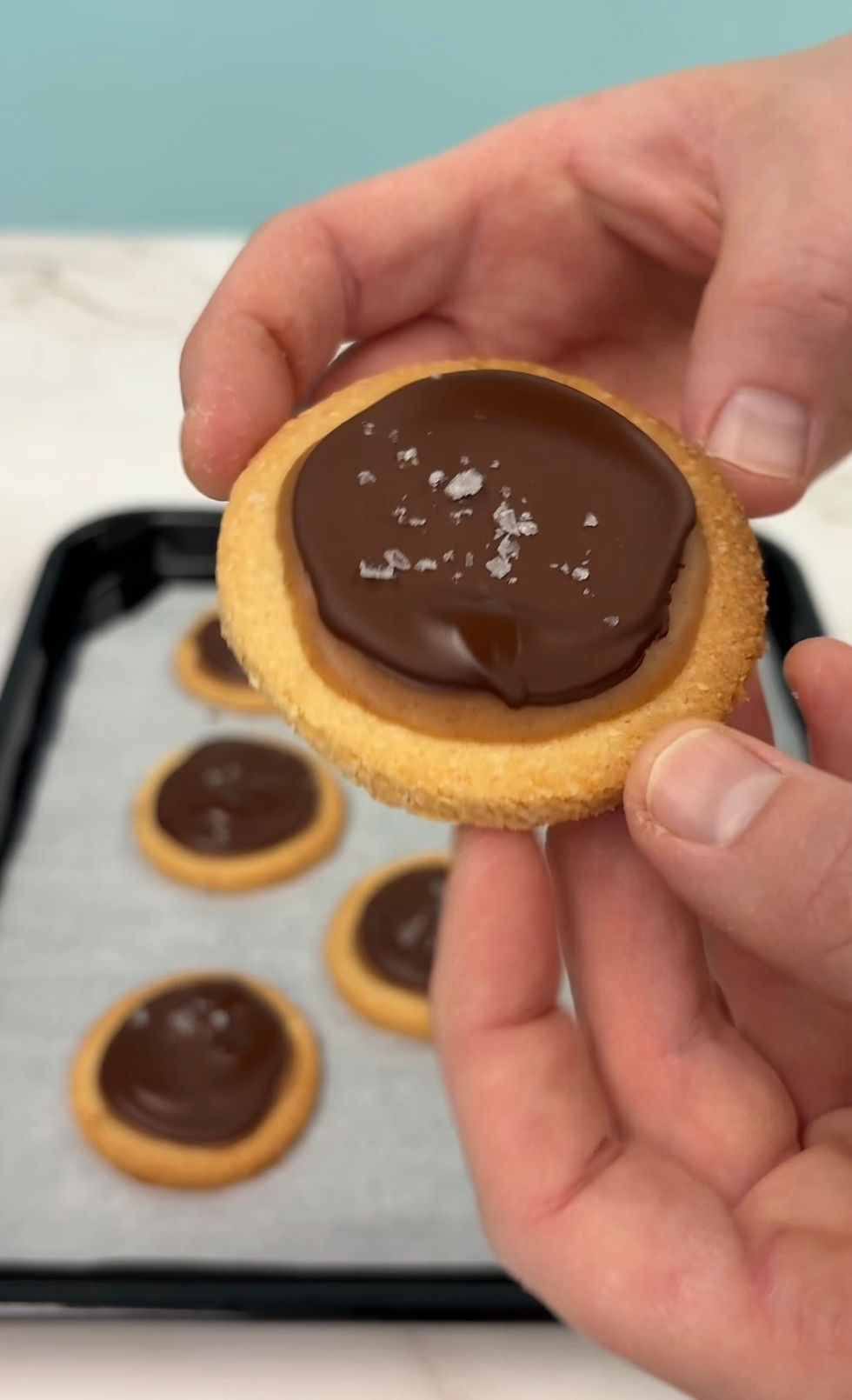 hand holding up a twix cookie: a gluten-free shortbread cookie, topped with a homemade caramel sauce, and crispy chocolate topping, and flakey sea salt