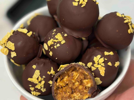 a white bowl stacked full of chocolate covered butterfinger cornflake peanut butter balls