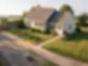 Aerial view of a ranch house with gray siding, garden beds, and a sidewalk along a quiet road.