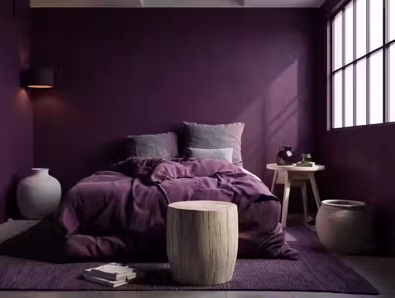 Camera da letto contemporanea con pareti color prugna scuro, biancheria da letto viola coordinata, arredi minimalisti in legno e morbida luce naturale da una grande finestra.