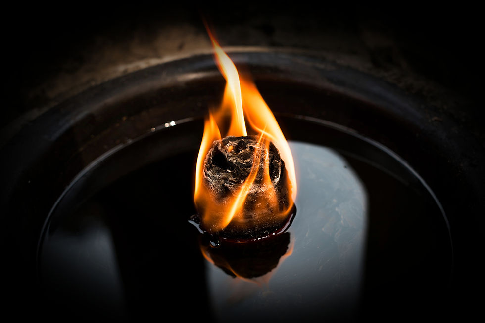A single flame dancing atop a temple oil lamp, reflecting in the still surface below — a quiet offering of light in sacred space.