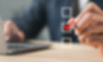 Blurred image of a persons torso sitting at a desk with a laptop, holding a hand up with a pen, checking one of three boxes shown.