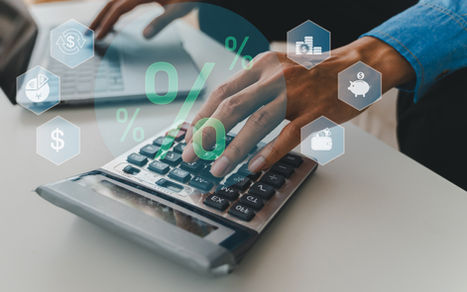 Hand calculating on a desk with green 0% finance icons and money symbols over a calculator.