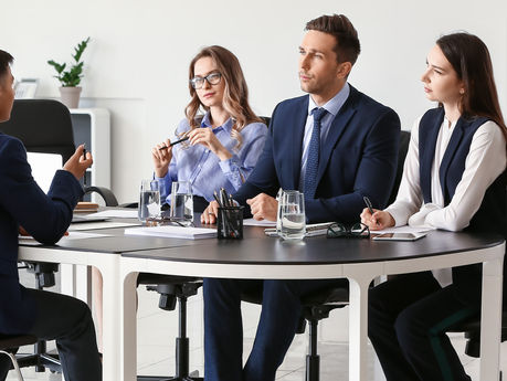 Business interview in a bright office: a man faces three suited individuals at a table