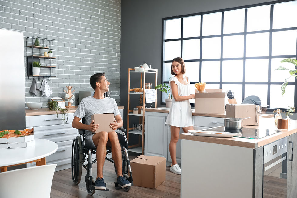 Smiling couple unpacking boxes in a bright modern kitchen, with a man in a wheelchair holding a box.