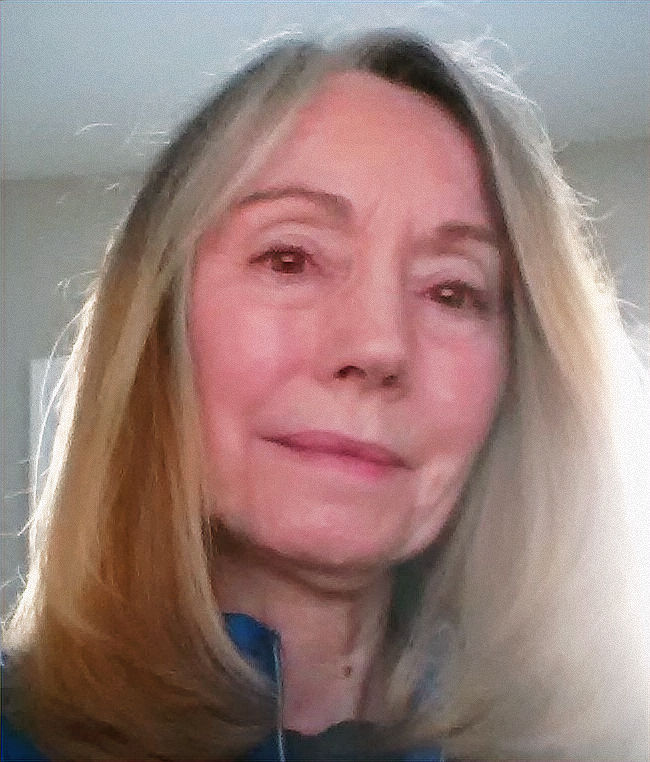 Close-up of a woman with long blonde hair looking at the camera indoors with a neutral expression.