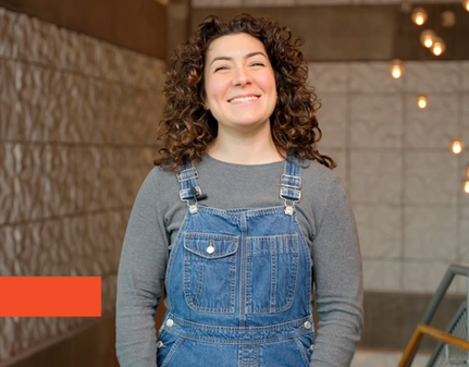 Smiling person in denim overalls, gray shirt.