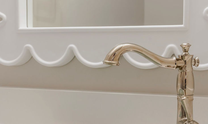 Playful powder room detail featuring a soft aqua sink with gold accents, scalloped mirror, and polished chrome faucet.