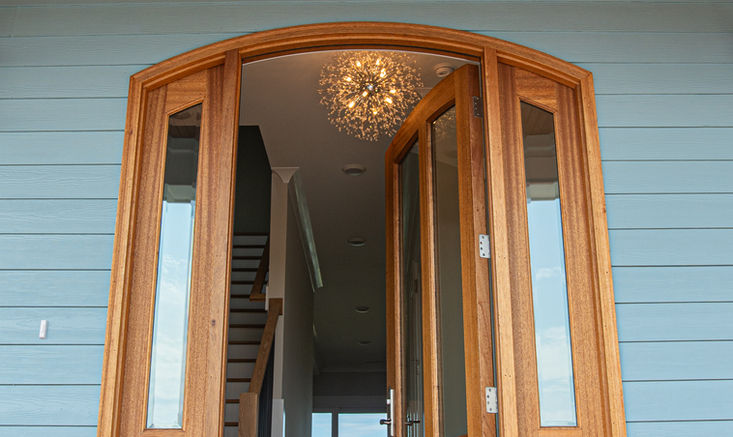 Arched front entry with wood door, vertical glass sidelights, and covered porch with tongue-and-groove ceiling.