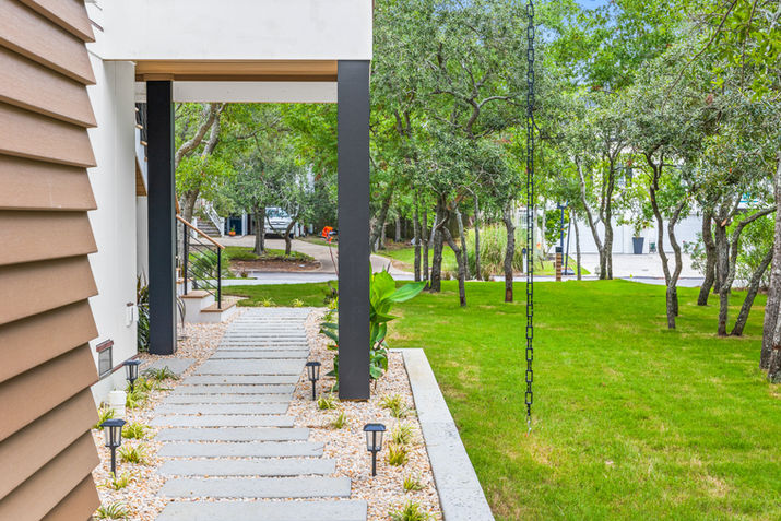 Side walkway of a modern coastal home with pavers, gravel landscaping, and mature trees.