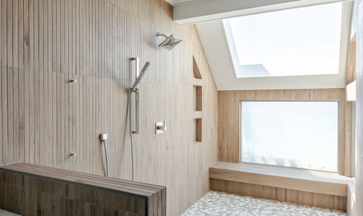 Walk-in shower with wood-look tile, built-in bench, pebble flooring, and skylight for natural light.