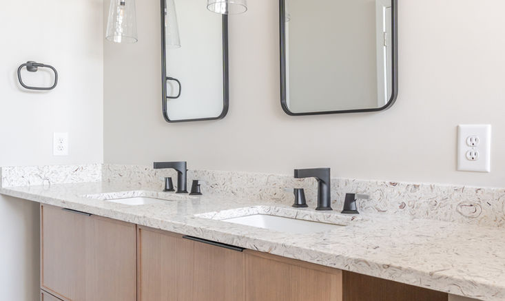 Minimal bathroom vanity featuring white oak cabinetry, a light quartz surface, and matte black fixtures paired with glass sconces.
