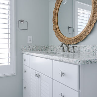 Bathroom vanity with white louvered cabinetry, large scalloped mirror, and brushed nickel fixtures, showcasing elegant interior design in Eastern NC.