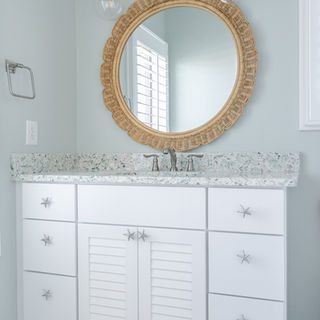 White bathroom vanity with louvered doors, scalloped mirror, and brushed nickel fixtures in an Eastern NC home.
