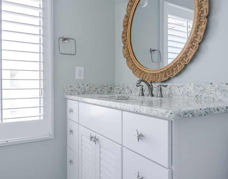 Playful coastal vanity with white cabinetry, terrazzo surface, woven mirror, and starfish hardware details.