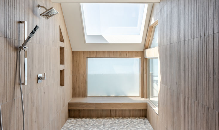 Spa-inspired shower with warm wood-look tile, built-in bench, pebble floor, and overhead skylight bringing in natural light.