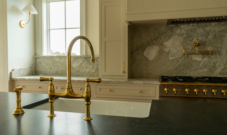 Custom kitchen with brass bridge faucet, black stone countertops, marble backsplash, and wall-mounted pot filler in an Eastern North Carolina custom home.