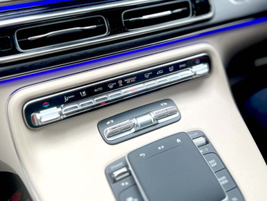 Close-up of a Mercedes-Benz V-Class dashboard featuring brushed aluminum controls, beige leather trim, and blue ambient LED lighting.