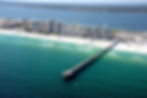 Aerial view of the Navarre Pier extending into the Gulf of Mexico, noted as the longest pier in the area, with beachfront buildings lining the picturesque shoreline of Navarre, Florida.