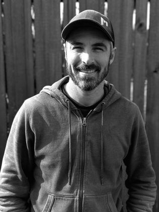 Black & White photo of one of our carpenters, Michael Thayer, smiling in front of a wooden fence.