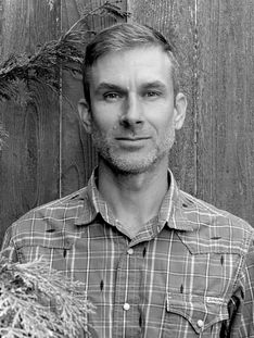 Black & White photo of owner, Zeke McFadin, in front of a wooden fence.