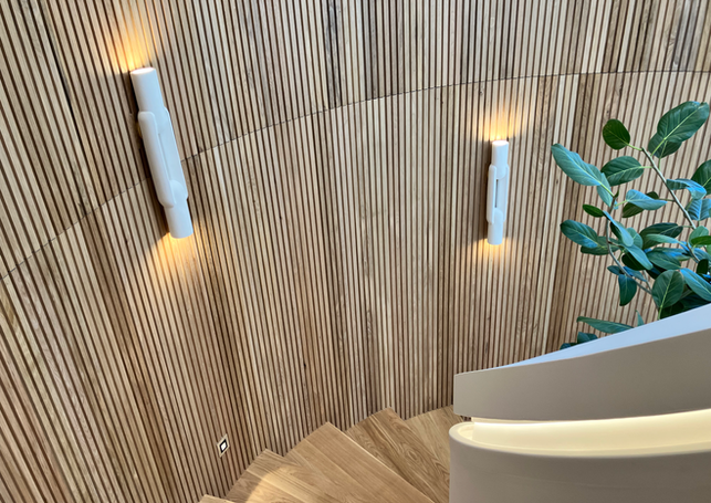 Looking down remodeled spiral staircase with custom oak slat walls, lighted grab rail, stair lights, and modern white sconces.
