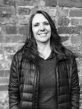 Black & White photo of our office manager, Holly Christiansen, smiling in front of a brick wall.