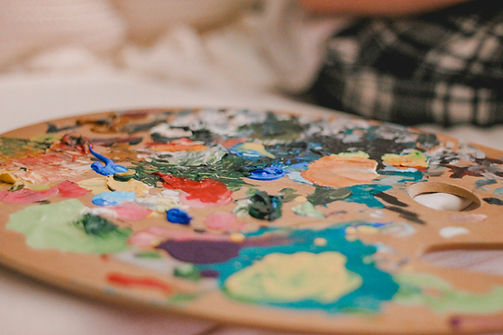 Close-up of a painter's palette filled with vibrant acrylic paints in various colors, including red, blue, green, and orange, with a blurred background.