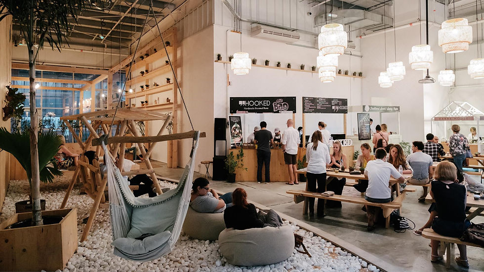 People socialize in a cozy cafe with hammock chairs and wooden benches. Soft lighting and hanging lamps create a relaxed atmosphere.