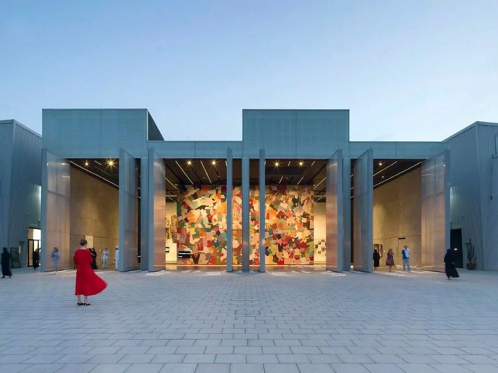 Modern art gallery entrance with people, large colorful mural inside. Pale blue walls, open airy space, woman in red dress in foreground.