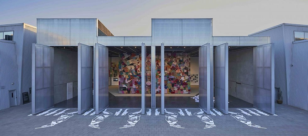Modern building with large open doors, colorful abstract mural inside. White floor patterns lead to entrance. Gray metallic exterior.